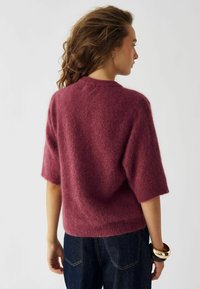Rundhalsets, kortærmet sweater i struktureret burgunder strik. Løs pasform, blødt materiale. Båret med mørk denim og stablede armbånd på håndleddet.