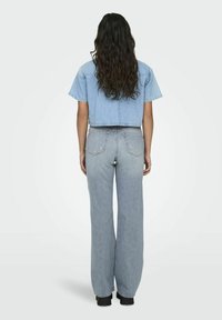 Heledat sinine lühikeste varrukatega denim jakk, mis on lühike ja sobitatud kõrge taljega heledate siniste laiade pükstega. Tekstuur tundub sile ja mugav.