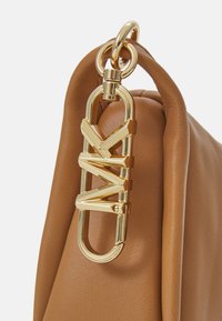 Handtasche aus tanfarbenem Leder mit goldenen Metallakzenten, auf denen die Buchstaben "MK" deutlich zu sehen sind. Sanfte Textur mit runder Form.