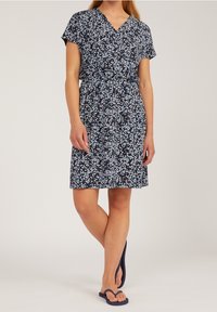 Navy sukienka w kwiatowy wzór z dekoltem w serek i krótkimi rękawami, wciągnięta w talii paskiem. Połączona z ciemnymi klapkami.