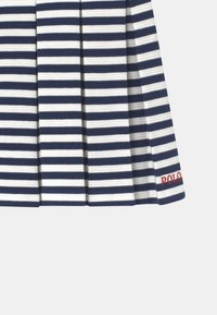 Granatowo-biała spódnica plisowana z miękką teksturą; z czerwonym logo "POLO" na końcu.