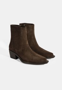 Bottines en suede marron avec un bout légèrement pointu, des fermetures éclair sur les côtés et un petit talon carré. Détails de couture verticale sur les côtés.