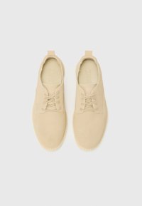 Beige suede lace-up shoes with round toe and stitching accents. Features a tonal pull tab at the heel and rubber sole for traction.
