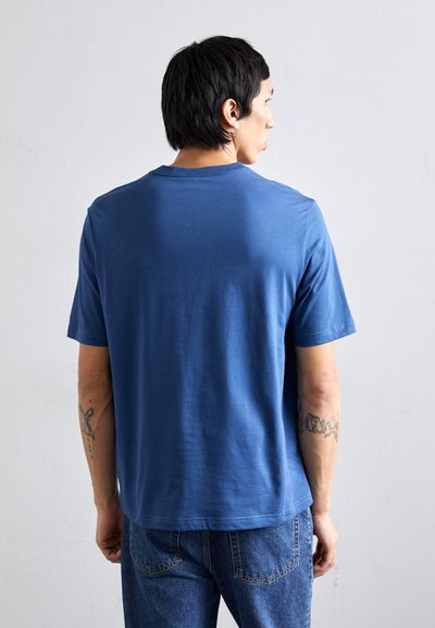 Mėlynas medvilninis marškinėlis su klasikinio apvalaus iškirpimo dizainu, trumpomis rankovėmis ir laisvu siluetu. Lygi tekstūra su subtiliais siuvinėjimo detalėmis.