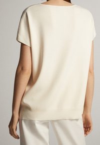 Kermansävyinen löysä yläosa, jossa lyhyet hihat, resorireunus ja sileä pinta, esittelee yksinkertaisen, minimalistisen mallin.