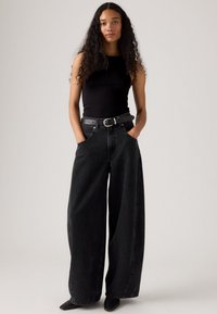 Czarna prążkowana bluzka bez rękawów w połączeniu z szerokimi czarnymi dżinsami i czarnym paskiem. Strój charakteryzuje się luźnym krojem i gładką fakturą.