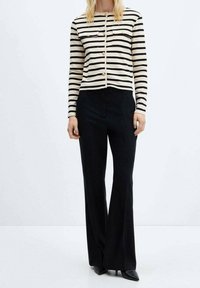 Pasiasty czarno-kremowy kardigan z złotymi guzikami, zestawiony z czarnymi rozszerzanymi spodniami i czarnymi szpilkami z zaostrzonym noskiem.