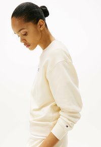 Crème sweatshirt met geribbelde manchetten, ronde hals en geborduurd logo op de borst. De stof lijkt zacht en heeft een losse pasvorm.