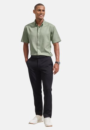 Hellgrünes kurzärmliges Shirt mit Knöpfen, kombiniert mit schwarzen Hosen und weißen Sneakers. Einfaches Design, glatte Textur und lässige Passform.