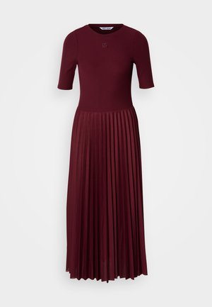 Burgundijas krāsas plisētā kleita ar īsām piedurknēm, pieguļošu augšu un apaļu izgriezumu. Satur faktūru audumu un diskrētu logo detaļu.