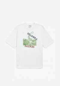 T-shirt bianca in cotone con una stampa grafica verde e rossa di un giocatore di tennis e il testo "DIADORA PALMAES" in blu e rosso. Maniche corte.
