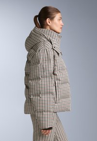 Jakna s mekim podstavom u smeđoj, krem i burgund bojama, visokog ovratnika i istaknutom kapuljačom, s bočnim džepovima i prilagođenim siluetom.