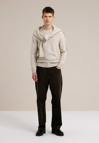 Bež pleteni džemper slojevit s odgovarajućim šal, uparen s tamno smeđim hlačama i crnim cipelama. Jednostavne, čiste linije, bez vidljivih uzoraka.