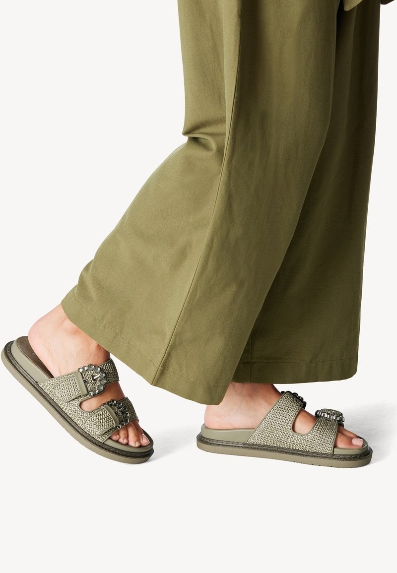 Platta sandaler med två breda tygremmar, olivgrön färg, texturerad vävdetalj och dekorativa spännen; sulan är dämpad och flexibel.