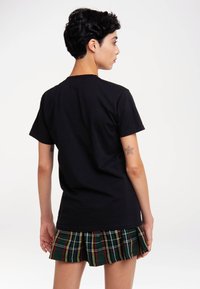 Black cotton t-shirt with a crew neck, paired with a green plaid pleated skirt featuring red and yellow accents visible at the hem.