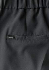 Schwarzer Stoff mit glatter Textur verfügt über eine gestickte Tasche und ein kleines Markenetikett. Das Design ist minimalistisch ohne Muster oder Akzente.