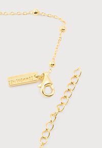 Χρυσή αλυσίδα με στρογγυλές χάντρες, κούμπωμα σε σχήμα αστακού και ορθογώνια ετικέτα με εγχάραξη "COMMONLINES" και κωδικό ημερομηνίας.