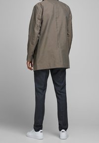 Långärmad skjorta med rutmönster i brunt och beige, kombinerad med mörkgrå skräddarsydda byxor och vita sneakers med varumärkesdetaljer.