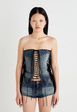 Denim korsett topp med snøring foran, svarte detaljer og frynser på sidene, sammen med blå denimshorts for et sammenhengende utseende.