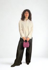 White long-sleeve shirt, black wide-leg pants, holding a small, textured pink beaded handbag. Simple design, contrast in color and materials.