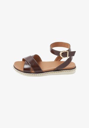 Sandalia plana de cuero marrón con correas cruzadas, hebilla en el tobillo, plantilla acolchada color beige y borde decorativo de cuenta blanca en la suela.