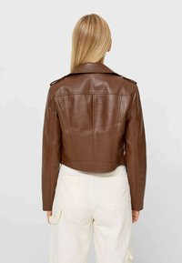 Brun cropped læderjakke med en glat tekstur, spidse krave og skulderlapper. Kombineret med lysebeige cargo-bukser.