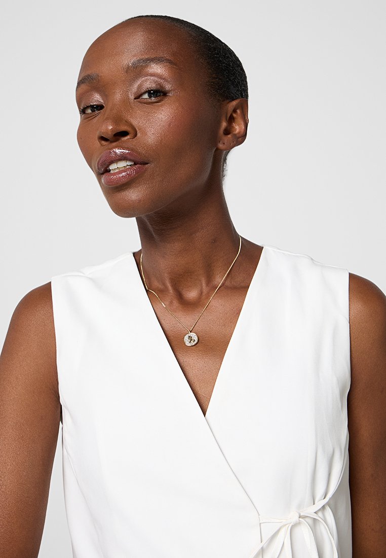 Abito avvolgente bianco con un dettaglio a fiocco, texture morbida e scollo a V profondo. La modella indossa una delicata collana d'oro con un pendente rotondo.