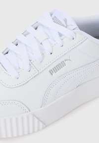Baskets blanches Puma avec une tige synthétique lisse, un bout rond, des lacets plats et une semelle texturée présentant des accents côtelés et des détails de logo.