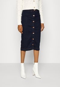 Denim pennkjol i mörkblått med knappstängning fram och kopparknappar. Kombinerad med en vit stickad tröja och vita klackade ankelboots.