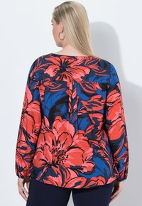 Maglietta a maniche lunghe con una vivace stampa floreale in rosso, blu e nero, realizzata in tessuto leggero con una vestibilità morbida e scollo rotondo.