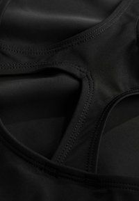 Černý sportovní top vyrobený z hladkého, vlhkost odvádějícího materiálu, s zakřiveným výstřihem a plochými švy pro pohodlí a odolnost.