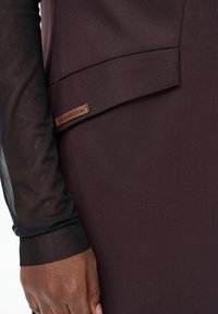 Brązowa sukienka z tkaniny o gładkiej fakturze; przezroczyste czarne rękawy z siateczki; po boku metka z napisem "blue shadow".