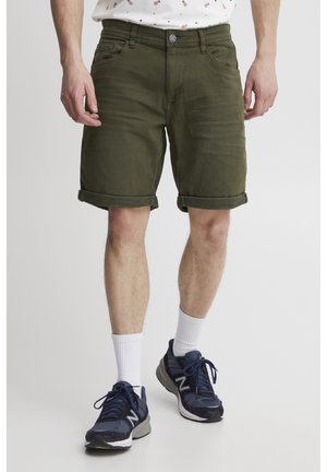 Olivgrüne Jeansshorts mit umgeschlagenen Säumen, Fronttaschen und Knopfverschluss. Getragen mit marineblauen Sportschuhen und weißen Crew-Socken.