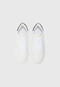 Baskets blanches avec un dessus en synthétique lisse, bout rond, semelle plate et lacets blancs. Présentent des accents noirs au talon et un marquage doré.