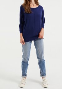 Tmavě modrý pletený svetr s kulatým výstřihem a tříčtvrtečními rukávy, v kombinaci se světle modrými džíny s ohrnutými nohavicemi a bílými teniskami.