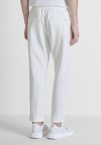 Witte elastische taillebroek met een taps toelopend ontwerp, voorzien van twee achterzakken en subtiele naden, samen met witte sneakers.