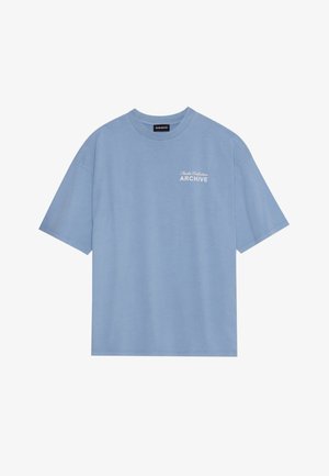 Sinine puuvillane T-särk ümarate krae ja lühikeste varrukatega. Vasakul rinnal on valge tekst "Studio Collection ARCHIVE".