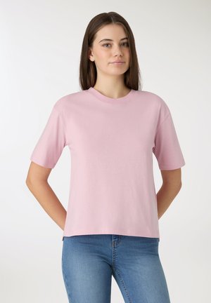 Jasnoróżowy t-shirt z krótkim rękawem i okrągłym dekoltem. Miękka tkanina, luźny krój i prosty design. W zestawieniu z dopasowanymi niebieskimi jeansami.