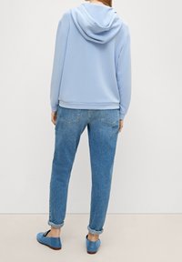 Felpa azzurra chiara con un ampio cappuccio, polsini e orlo a coste. Abbinata a jeans in denim a vestibilità ampia arrotolati alla caviglia e scarpe blu slip-on.