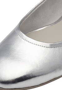 Gros plan sur une chaussure en cuir métallique argenté avec un bout arrondi et une doublure intérieure beige.