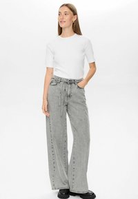 Jean large gris à taille haute, avec une ceinture nouée et des coutures contrastées subtiles. Associé à un haut blanc uni à manches courtes.