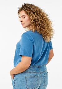 Camiseta de algodón azul con mangas cortas, escote redondo y corte relajado, combinada con unos vaqueros de mezclilla clara de cintura alta.