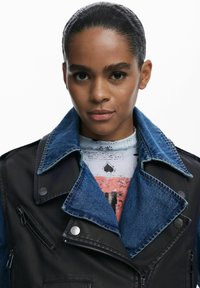 Giubbotto in pelle nera e denim con ampio colletto, chiusura con zip e design a due tonalità. Presenta bottoni metallici e tasche con zip.