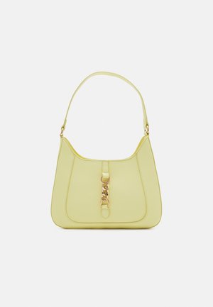 Gelbe Handtasche mit einem einzelnen Schulterriemen und einem goldenen Kettendetail in der vorderen Mitte vor schlichtem Hintergrund.