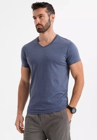 T-shirt blu a scollo a V in un tessuto morbido e leggero. Maniche corte e taglio aderente con una sottile texture. Indossato con pantaloni corti grigi e un orologio nero.