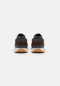 Braune Wildleder-Sportschuhe mit weißem Zwischensohle und Gummisohle. Merkmale sind blaue Stoffakzente und schwarze Fersendetails.