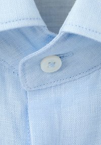 Close-up of a light blue shirt collar with a white button fastened through a buttonhole on textured fabric.