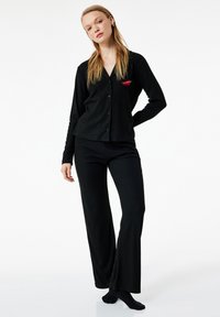 Sort ribbet pyjamasesæt med en knap-op langærmet bluse, der har en broderet rød chilipeber, samt matchende løstsiddende bukser.