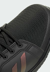 Scarpa da ginnastica nera con tomaia in tessuto testurizzato, accenti sintetici e strisce riflettenti. Presenta lacci rotondi e un design ergonomico.