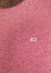 Červené melírované tričko s kulatým výstřihem. Obsahuje malé bílé a modré pruhované logo na hrudi. Vyrobeno z texturované bavlněné látky.